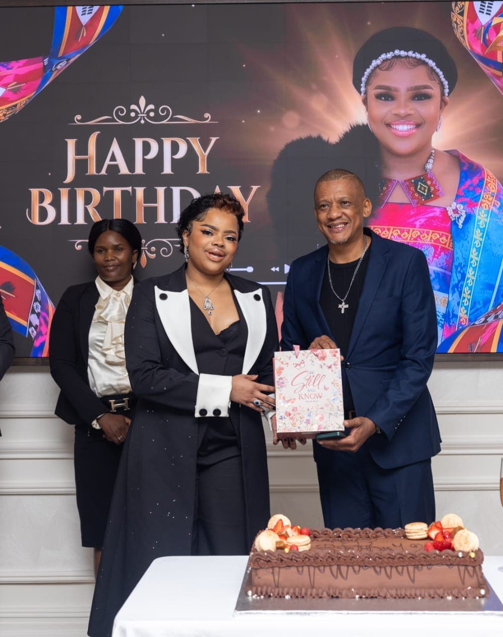 Dr. Keith Clint Harrington presenting a birthday gift to the Principal Princess beside her birthday cake